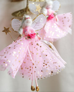 Decorative fairy ornament with pink tulle skirt and gold stars on a blurred background