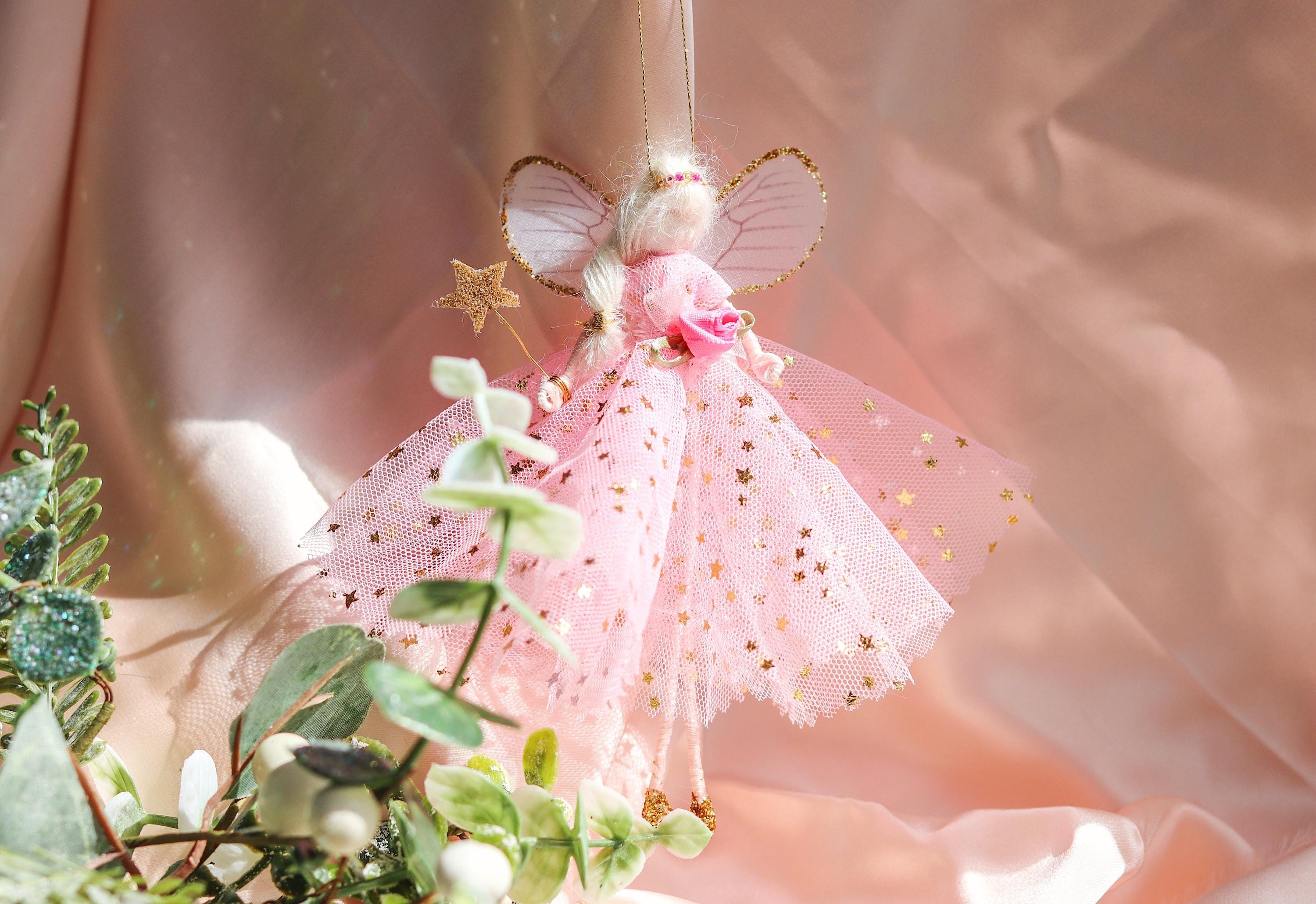 Decorative fairy figurine with pink dress and gold accents hanging among greenery.