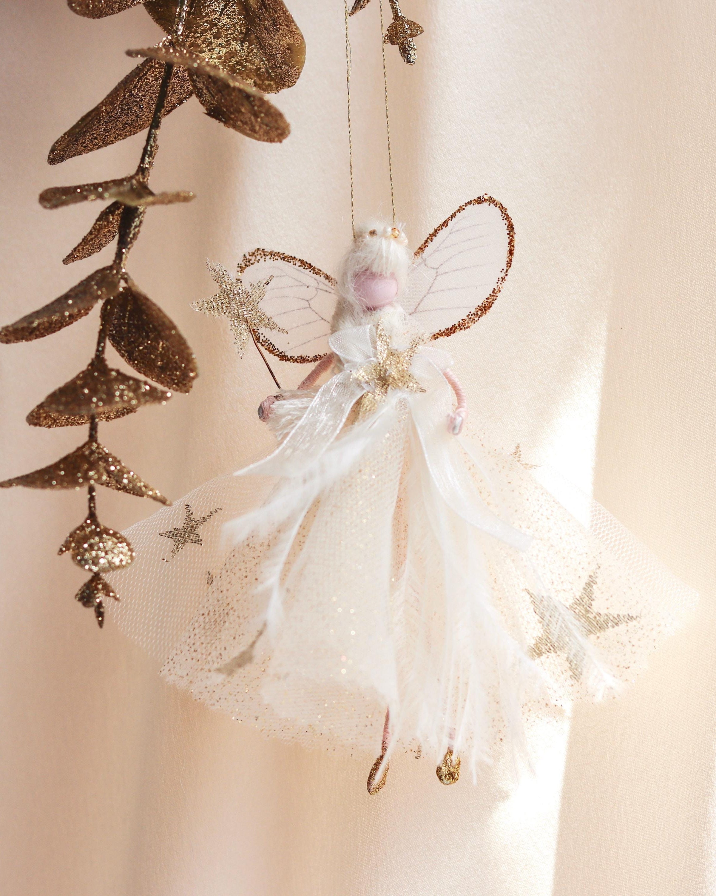 Decorative fairy hanging ornament with gold leaves on a soft beige background