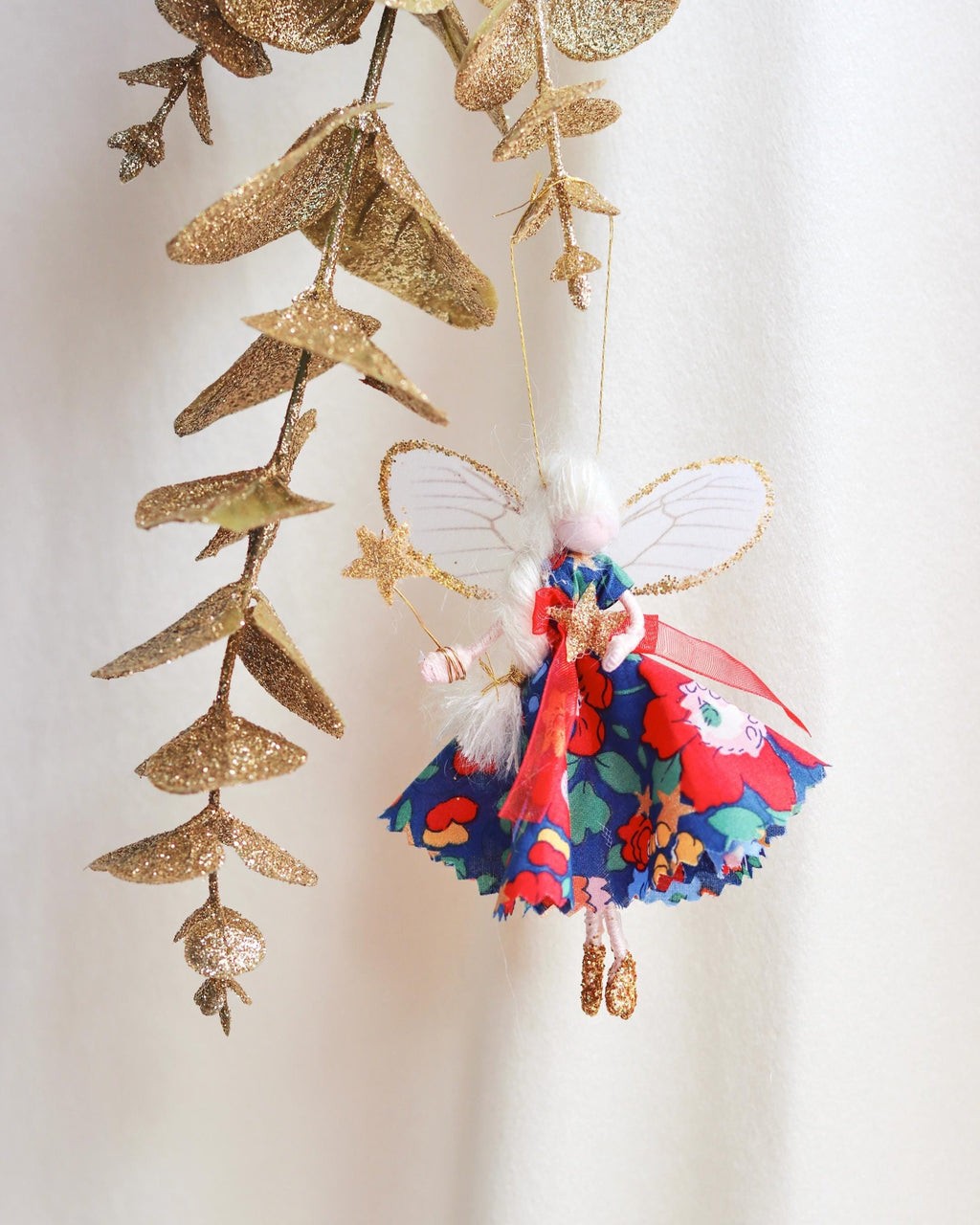 Decorative fairy figurine with colorful dress and glittery gold leaves on a light background