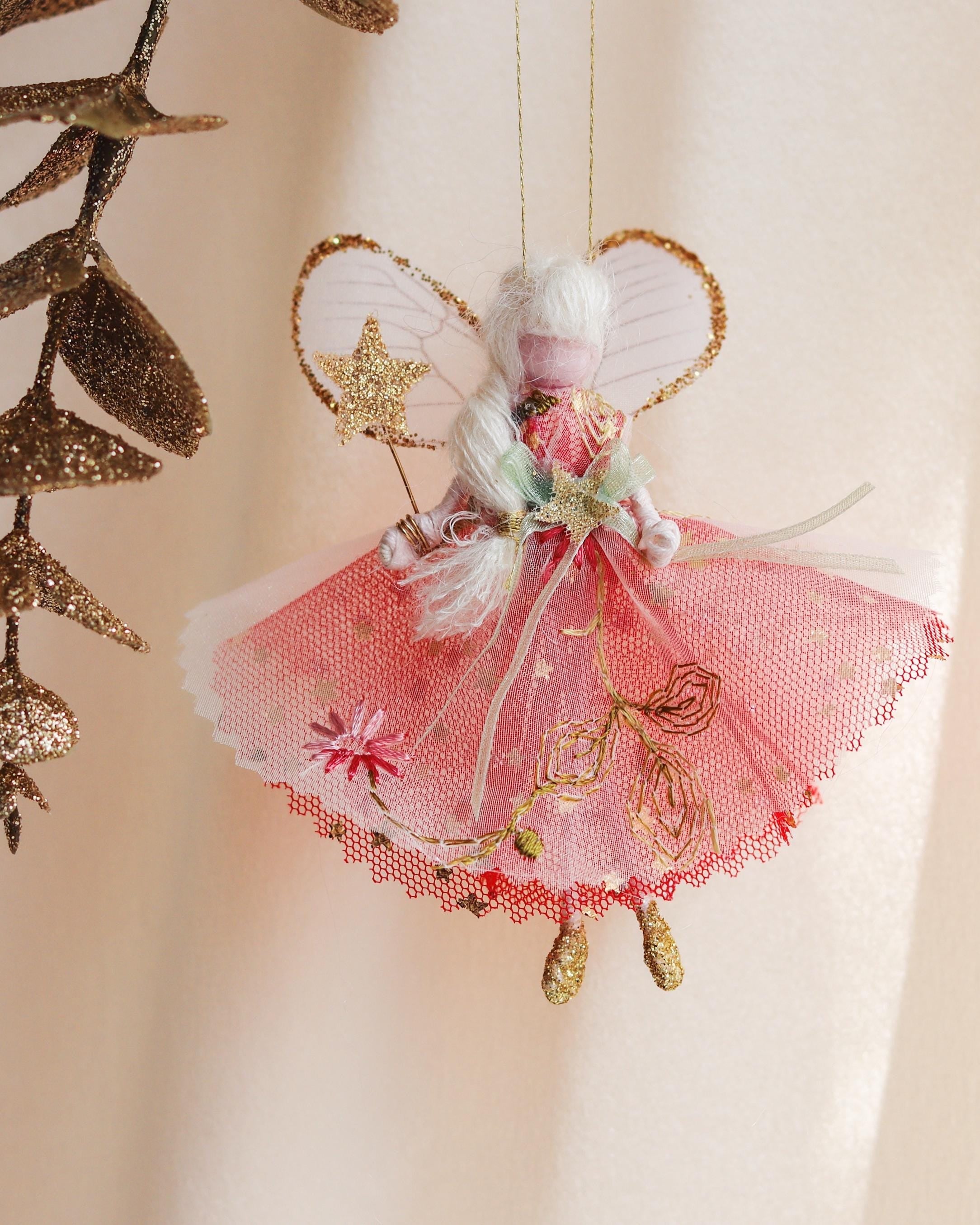 Decorative fairy ornament with pink dress and gold accents on a beige background