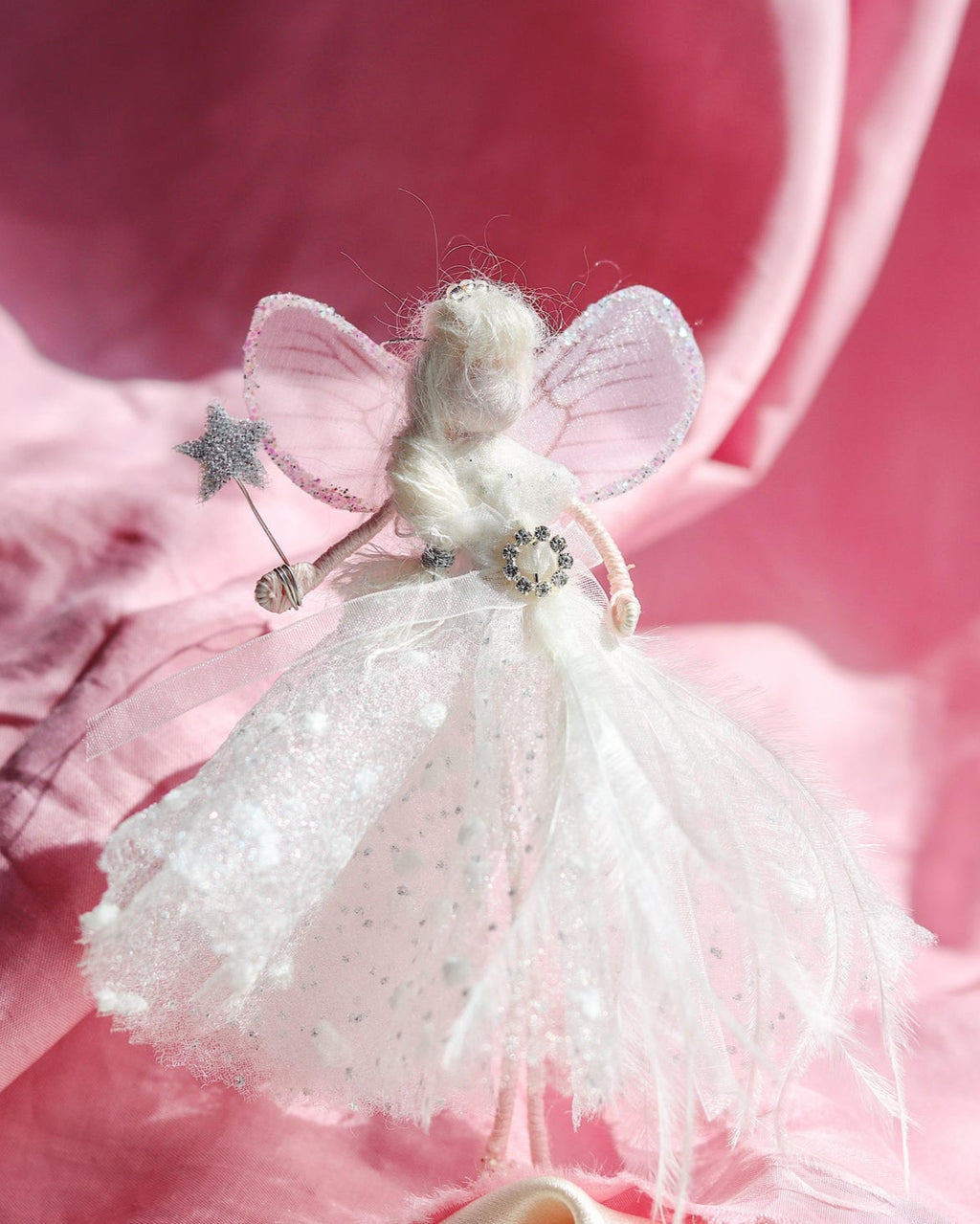 White fairy doll with pink wings on a pink background
