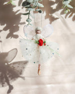 Load image into Gallery viewer, A delicate fairy ornament hanging from a green branch, featuring a small white-dressed fairy with translucent wings, a red flower at the waist, and a sparkly white tulle skirt against a softly lit background with leaf shadows.
