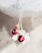 Load image into Gallery viewer, A close-up of a white lace and tulle fabric decoration with two small wrapped pink and white fabric flowers hanging from a string.
