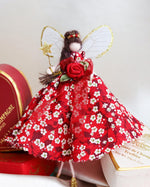 Load image into Gallery viewer, Valentine fairy decoration figurine in a red liberty print floral dress with a rose, standing next to a heart-shaped chocolate box on a white background.
