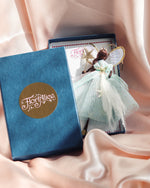 Load image into Gallery viewer, A decorative fairy ornament displayed next to its blue gift box on draped blush pink satin fabric. The box features a gold circular logo reading 'Floiralice'.
