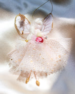 Load image into Gallery viewer, A decorative fairy ornament with translucent pink wings outlined in gold glitter, a white tulle dress with gold star accents, and a pink flower at the waist, shown on a soft satin-like background.
