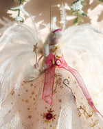 Load image into Gallery viewer, A decorative angel Christmas ornament with white feathers, a cream tulle dress with gold star details, and a pink ribbon bow, shown against a softly lit neutral background.
