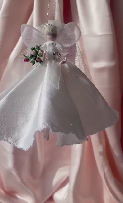 video of bridal fairy  figurine with a white dress on a soft pink background holding a miniature bouquet bridal gift, wedding present, new bride to be