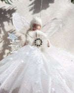 Load image into Gallery viewer, A white angel Christmas ornament with translucent wings, a fluffy white dress, and a black-and-white jeweled chest emblem, photographed against a light neutral background with soft shadows.
