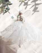 Load image into Gallery viewer, A white angel fairy Christmas ornament with translucent wings, a sparkly tulle dress, and a small star wand, hanging against a softly lit cream background with decorative greenery.
