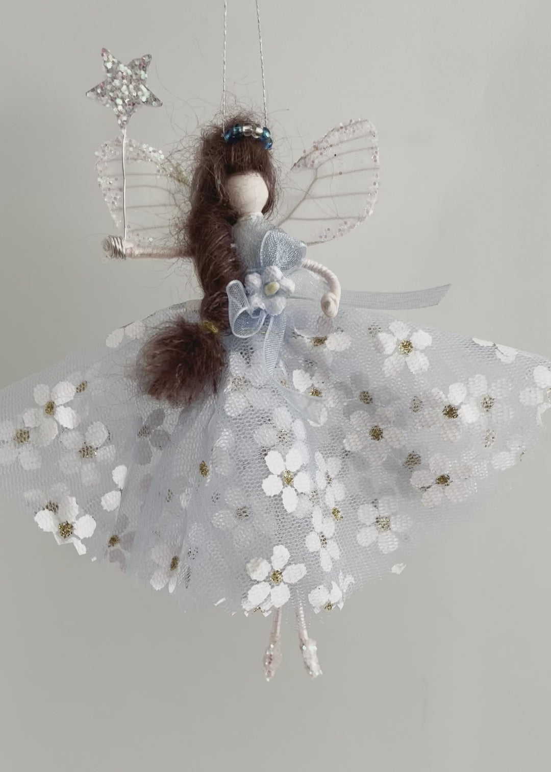 Dressed in a pale blue sparkly tulle with white flowers. She has sashed her gown at the waist with a pale blue Organza ribbon and a velvet forget-me-knot. Her little shoes are dipped in glitter, and upon her head sits a blue glass tiara. Her delicate wings are made from silk Organza and of course, her glittered wand that brings you never-ending memories!