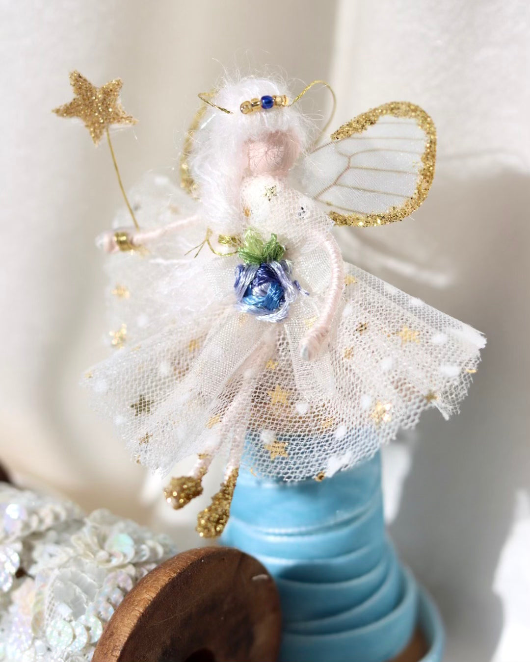 This little fairy is dressed in a Gold star and white polka dot gown. She has sashed her gown at the waist with an Organza ribbon and a little blue embroidered rose trim. She has little shoes dipped in glitter and of course, her glittered wand brings you never-ending memories!